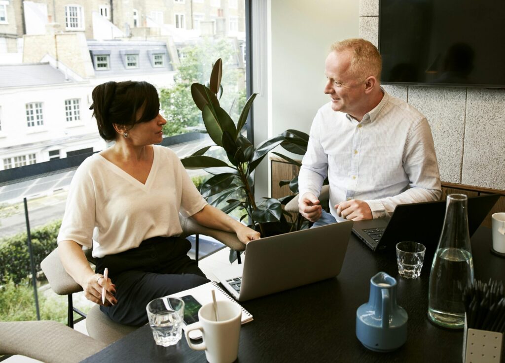 Two business professionals engaging in a team meeting in a modern London office with a large window view.